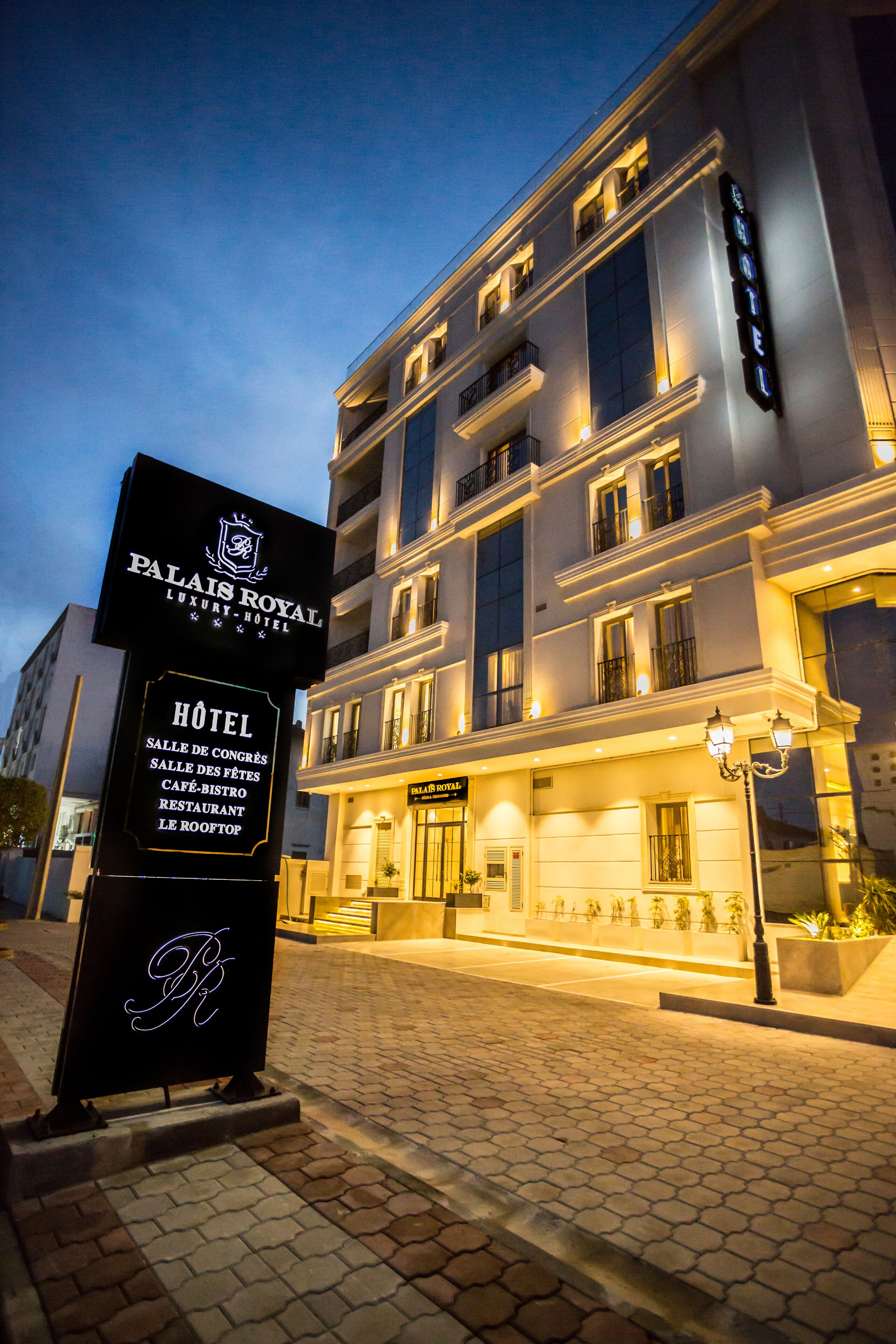 Entrada de hotel con un letrero que indica el nombre y los servicios.
