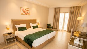 A hotel room with a large bed, two bedside tables with lamps, a chair, a desk with a lamp, and a window with curtains.