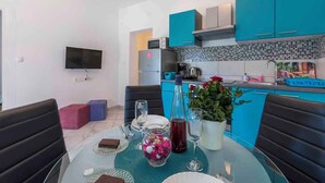 A modern kitchen with teal cabinets, a flat-screen TV, and a dining area with a glass table set for two. - Holiday apartment with barbecue for shared use (Crikvenica)