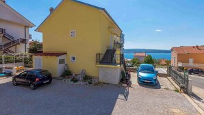 A yellow building with a staircase, two cars parked in front, and a view of the sea in the background. - Holiday apartment with barbecue for shared use (Crikvenica)