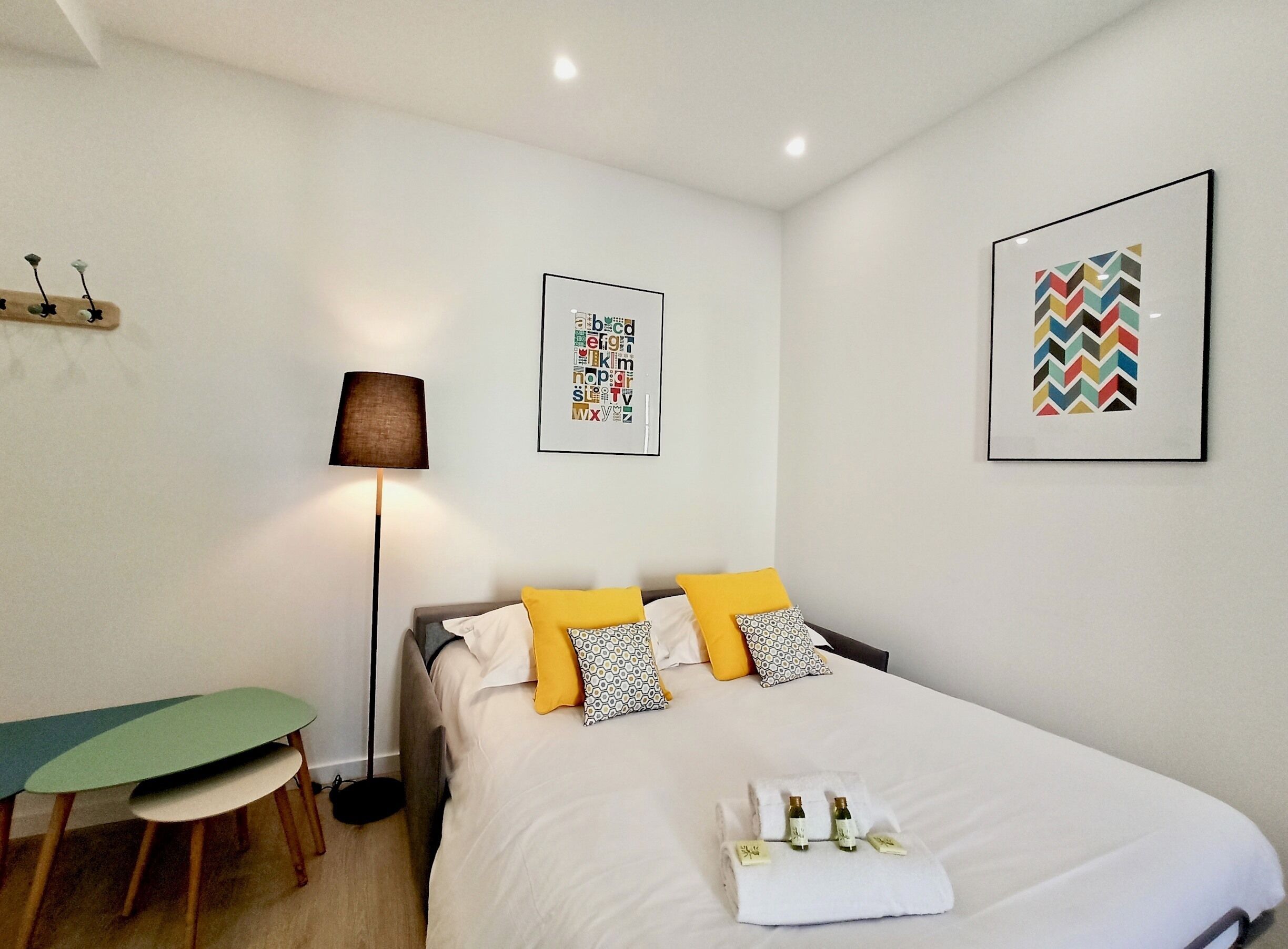 Una camera d'albergo ordinata con un letto, una scrivania e due opere d'arte appese alle pareti.