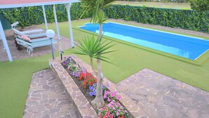 A swimming pool with a stone deck and a covered seating area with lounge chairs.