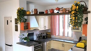A kitchen with a stove, oven, and various kitchen appliances. There is a window with curtains and a shelf above the counter holding kitchenware.
