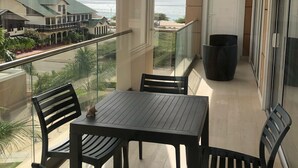Un balcón con mesa y sillas, con vistas a una playa y edificios.