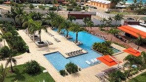 Un área de piscina en un resort, con varias piscinas, tumbonas y palmeras.