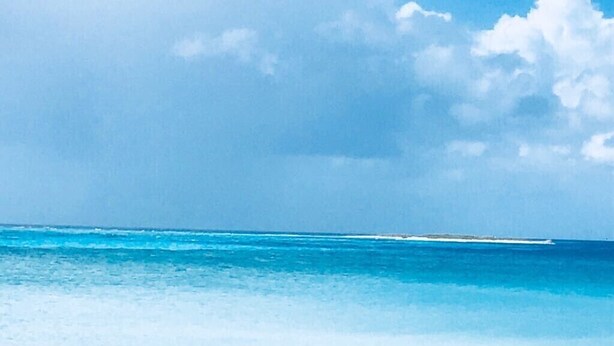 Una playa con agua azul cristalina y una costa lejana.