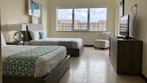 Habitación de hotel con dos camas, un escritorio, una silla, un televisor y una ventana con vistas a la ciudad.