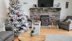 Un salon chaleureux avec un sapin de Noël blanc, une cheminée, un téléviseur à écran plat et un calendrier posé sur la cheminée.