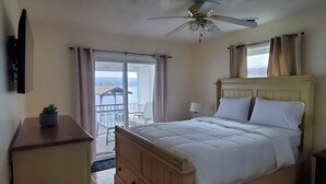 Une chambre avec un lit, un ventilateur de plafond, une commode et une vue par la fenêtre.