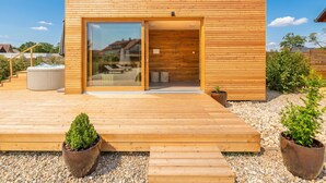Un bâtiment moderne en bois, doté d’une entrée avec une porte en verre, d’un jacuzzi et d’une terrasse en bois.