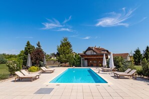 A rectangular swimming pool with lounge chairs and umbrellas, surrounded by a house and trees. - Villa Prleski Raj - Pool, Sauna, Jacuzzi (Križevci)