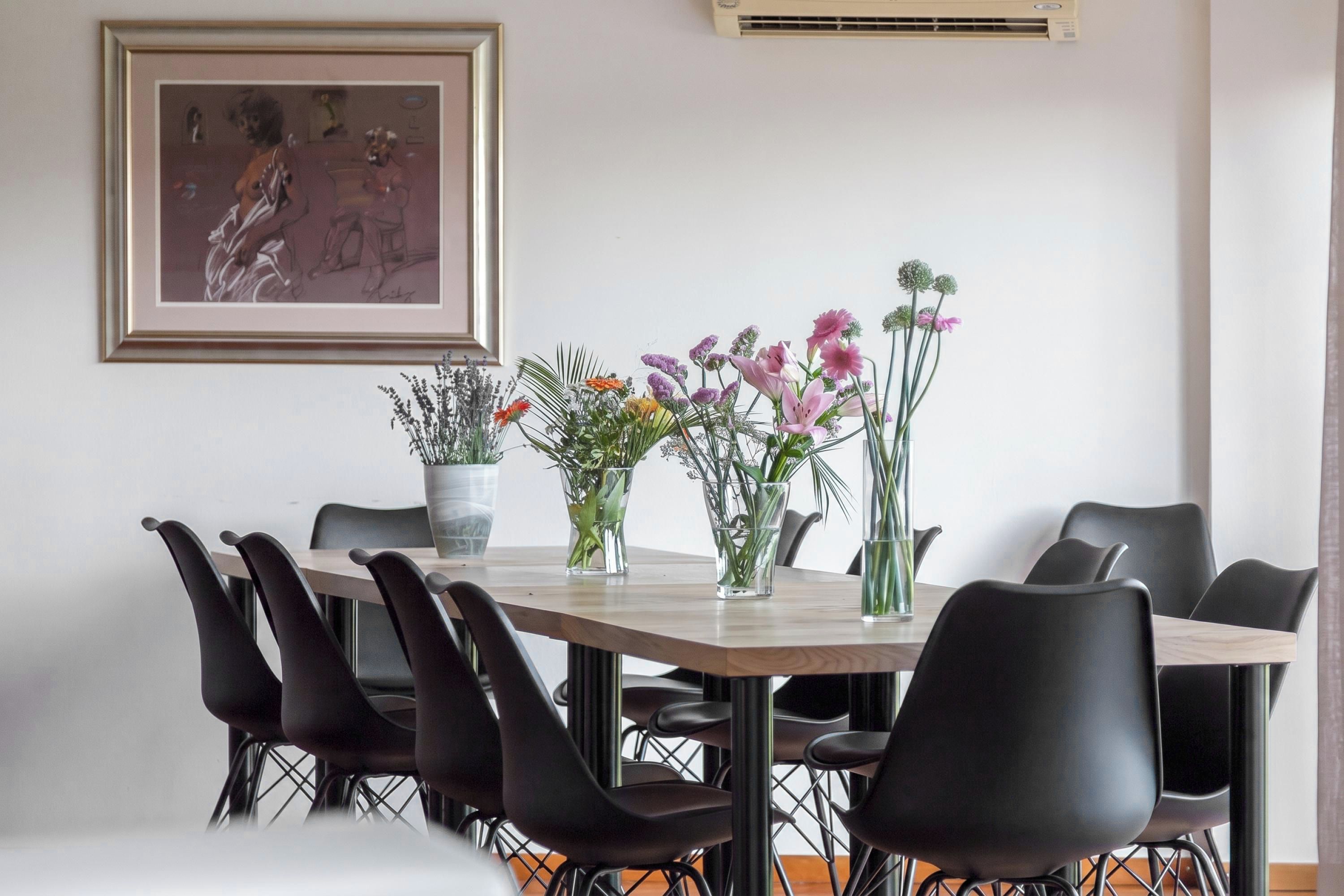Un comedor con una mesa de madera, sillas negras y centros de mesa con flores.