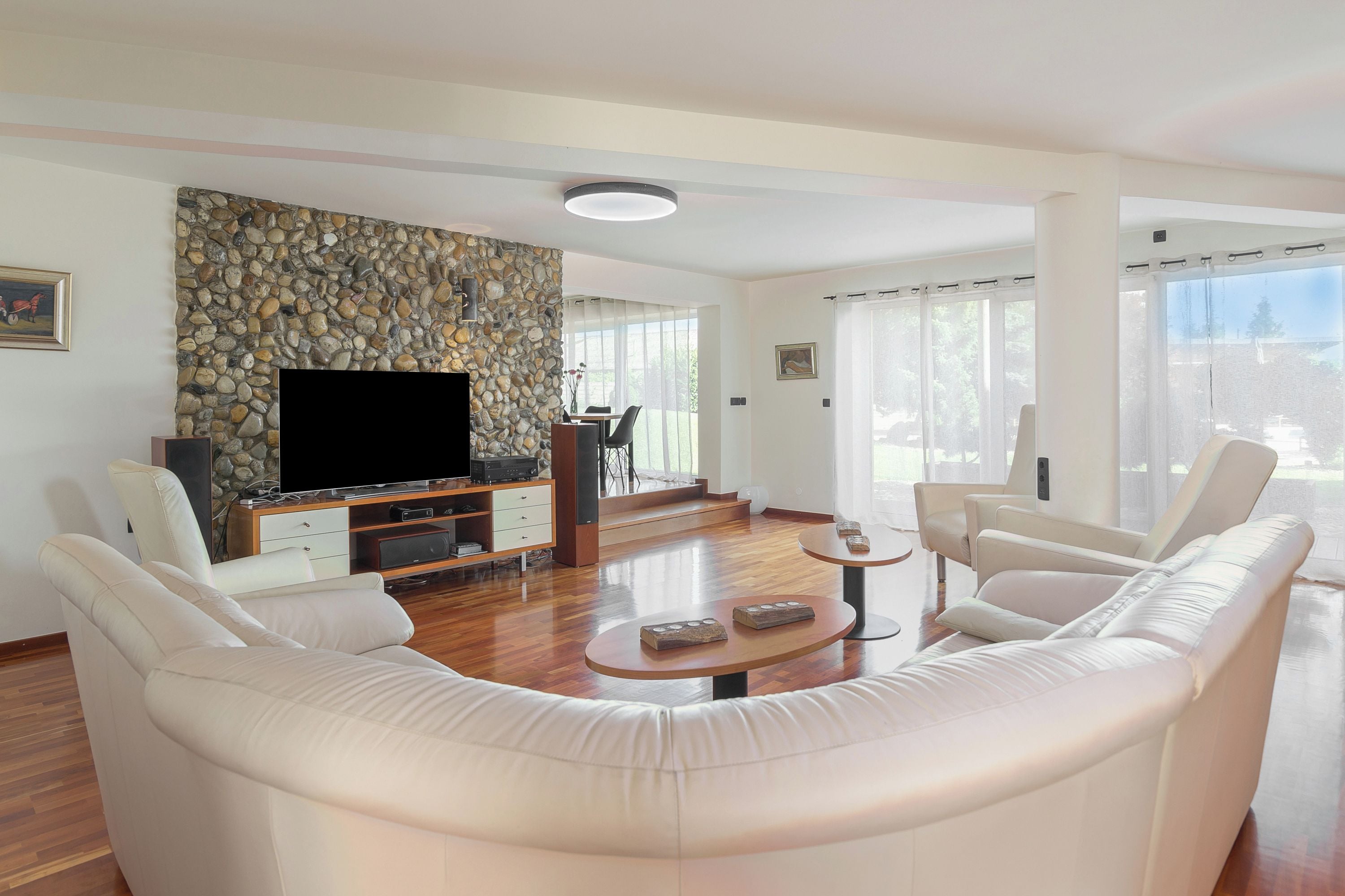 A modern living room with a stone wall, a flat-screen TV, a sofa, and a dining area.
