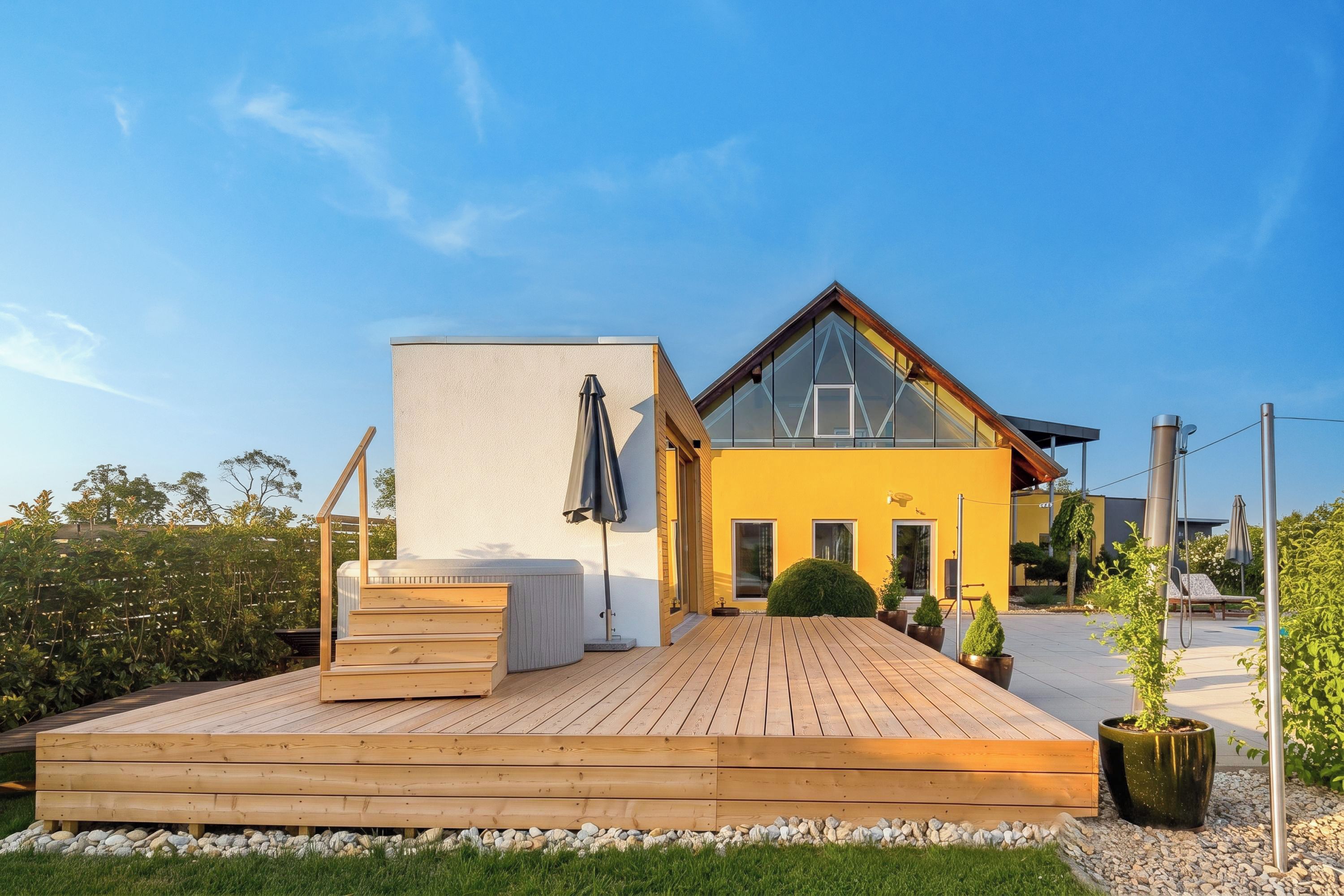 Una casa moderna con terraza de madera, un amplio ventanal y una pared exterior amarilla.