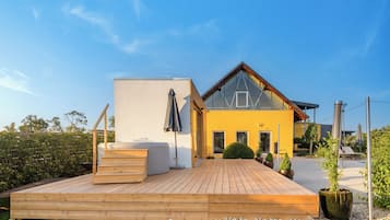 Una casa moderna con terraza de madera, un amplio ventanal y una pared exterior amarilla.