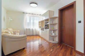 Une pièce avec un canapé, un plancher en bois, une bibliothèque, une porte et une fenêtre avec des rideaux.
