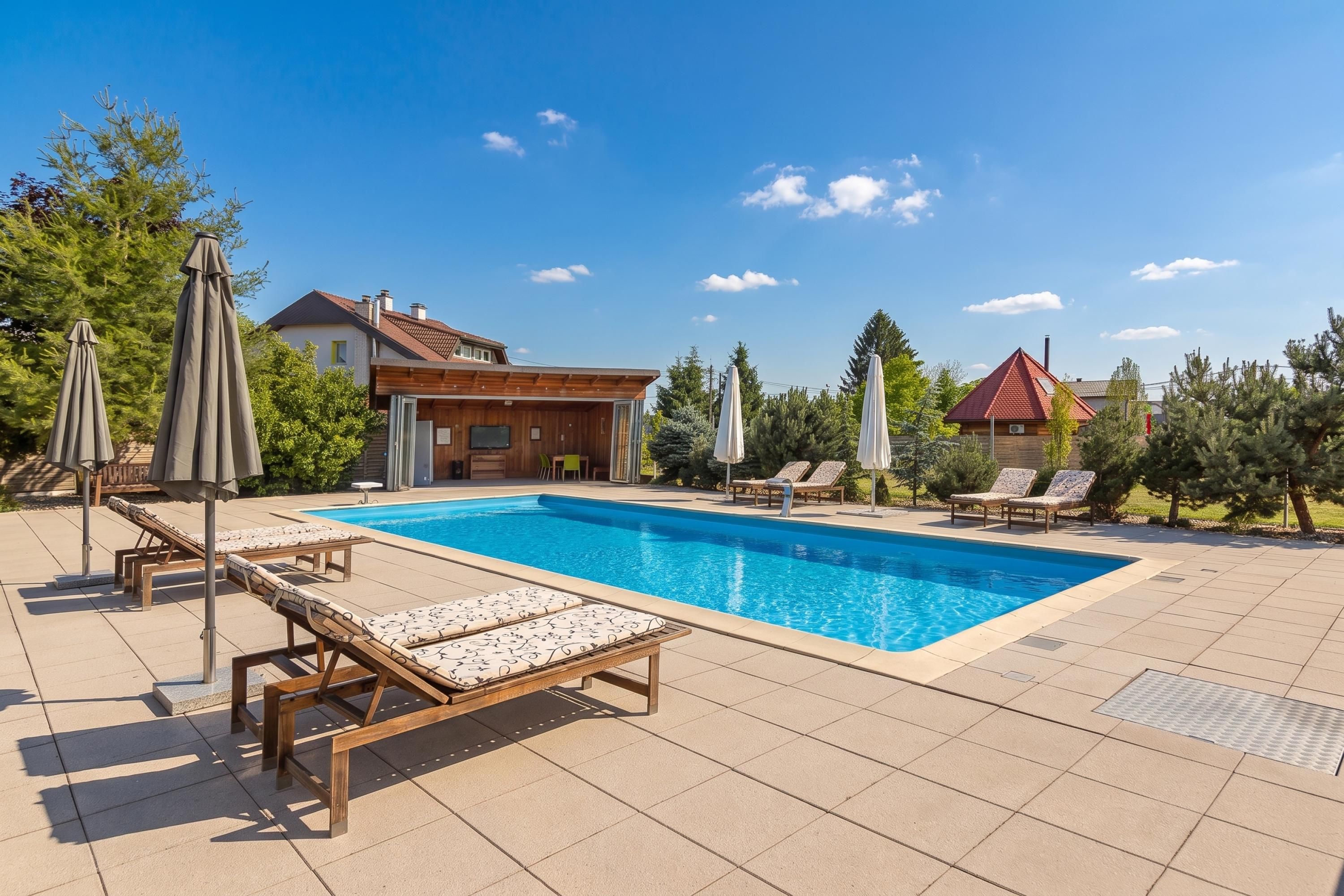 Una piscina con sillas de descanso, sombrillas y una casa al fondo.