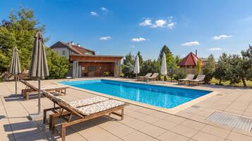 Una piscina con sillas de descanso, sombrillas y una casa al fondo.
