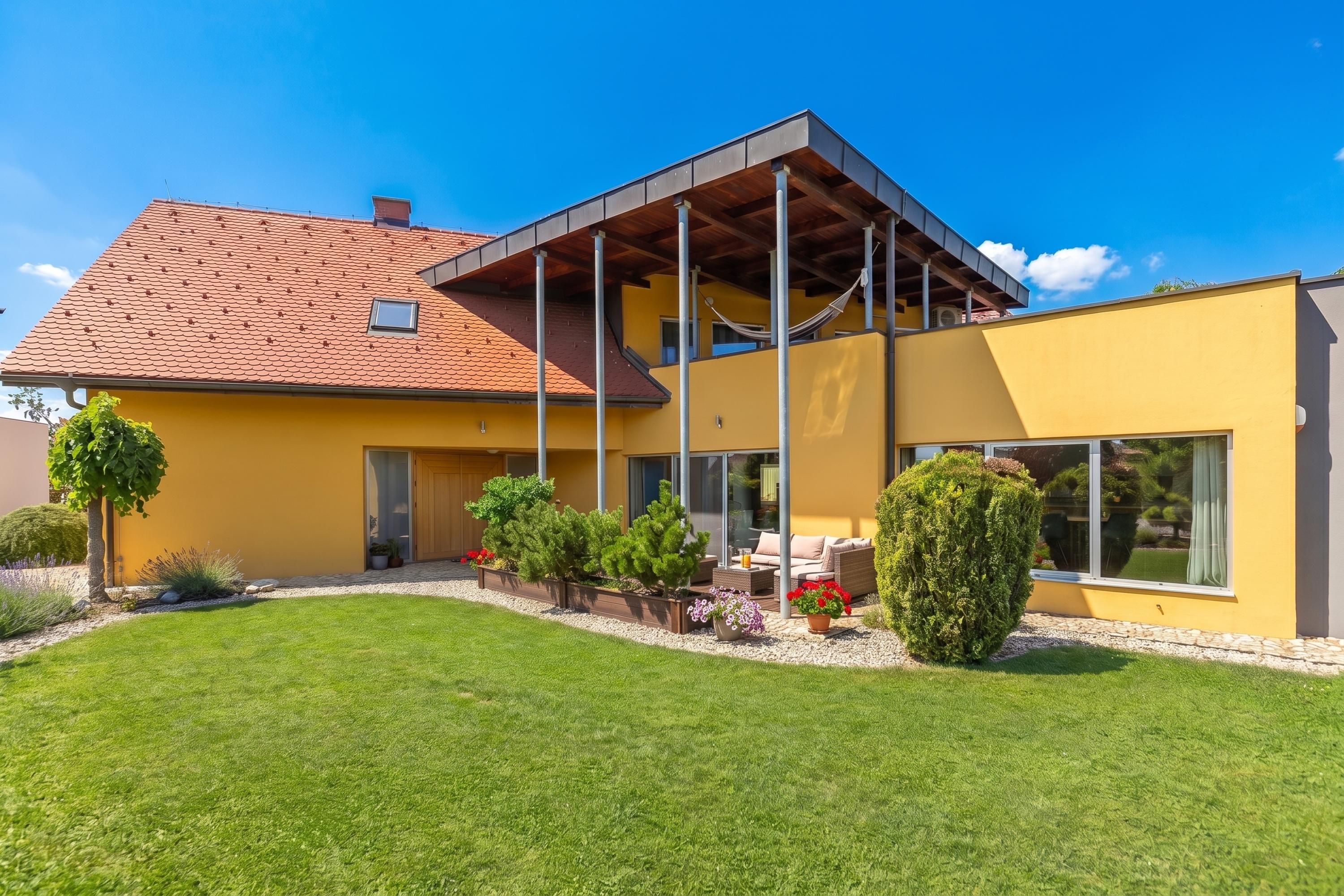 Una casa moderna con fachada amarilla, techo de tejas rojas y un patio cubierto.