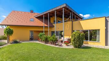 Una casa moderna con fachada amarilla, techo de tejas rojas y un patio cubierto.