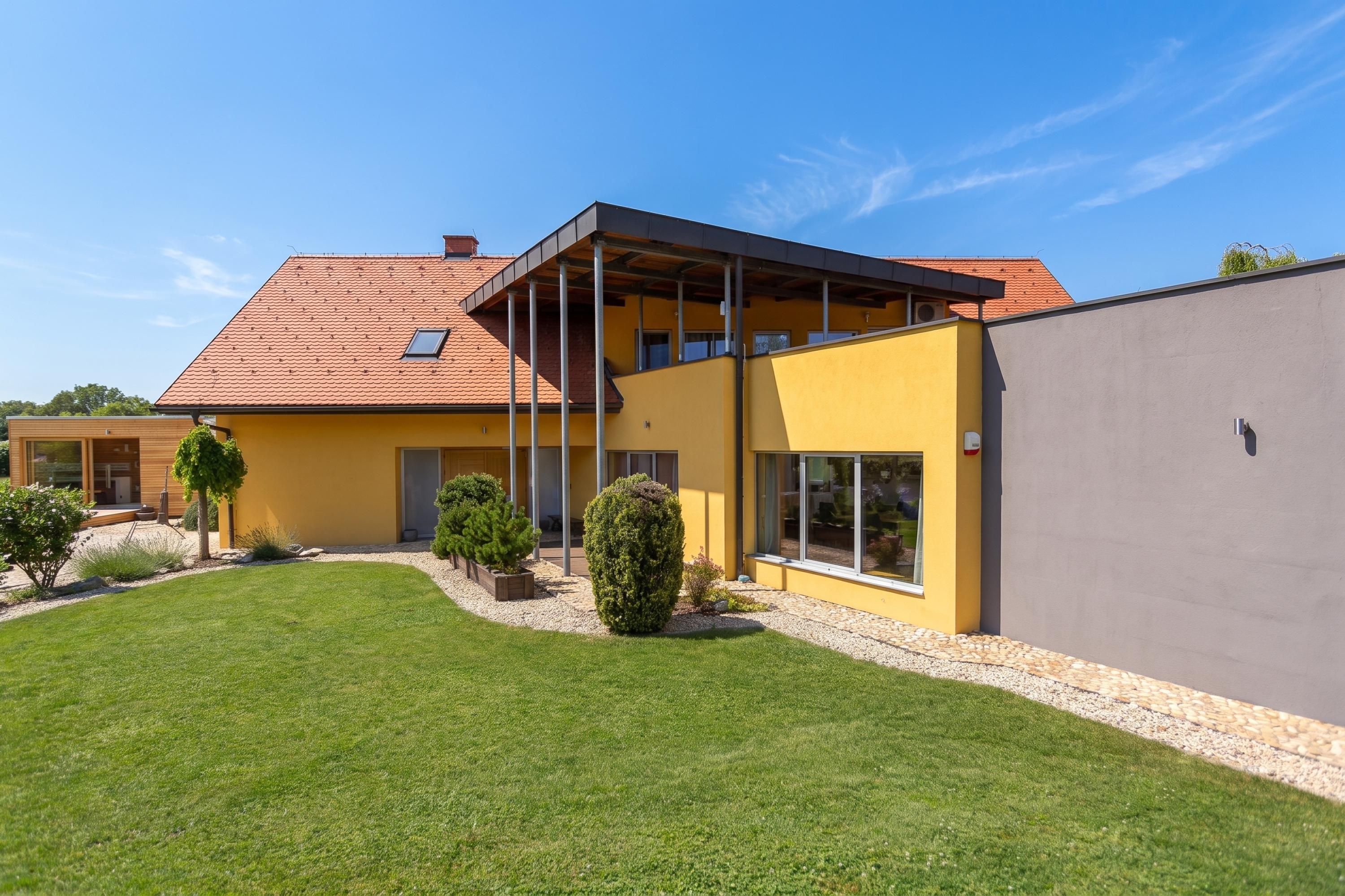 Una casa moderna de dos pisos con fachada amarilla, techo inclinado y un espacio exterior cubierto.