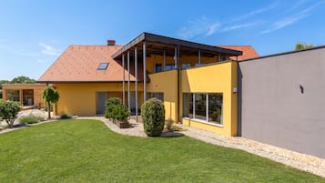 Una casa moderna de dos pisos con fachada amarilla, techo inclinado y un espacio exterior cubierto.