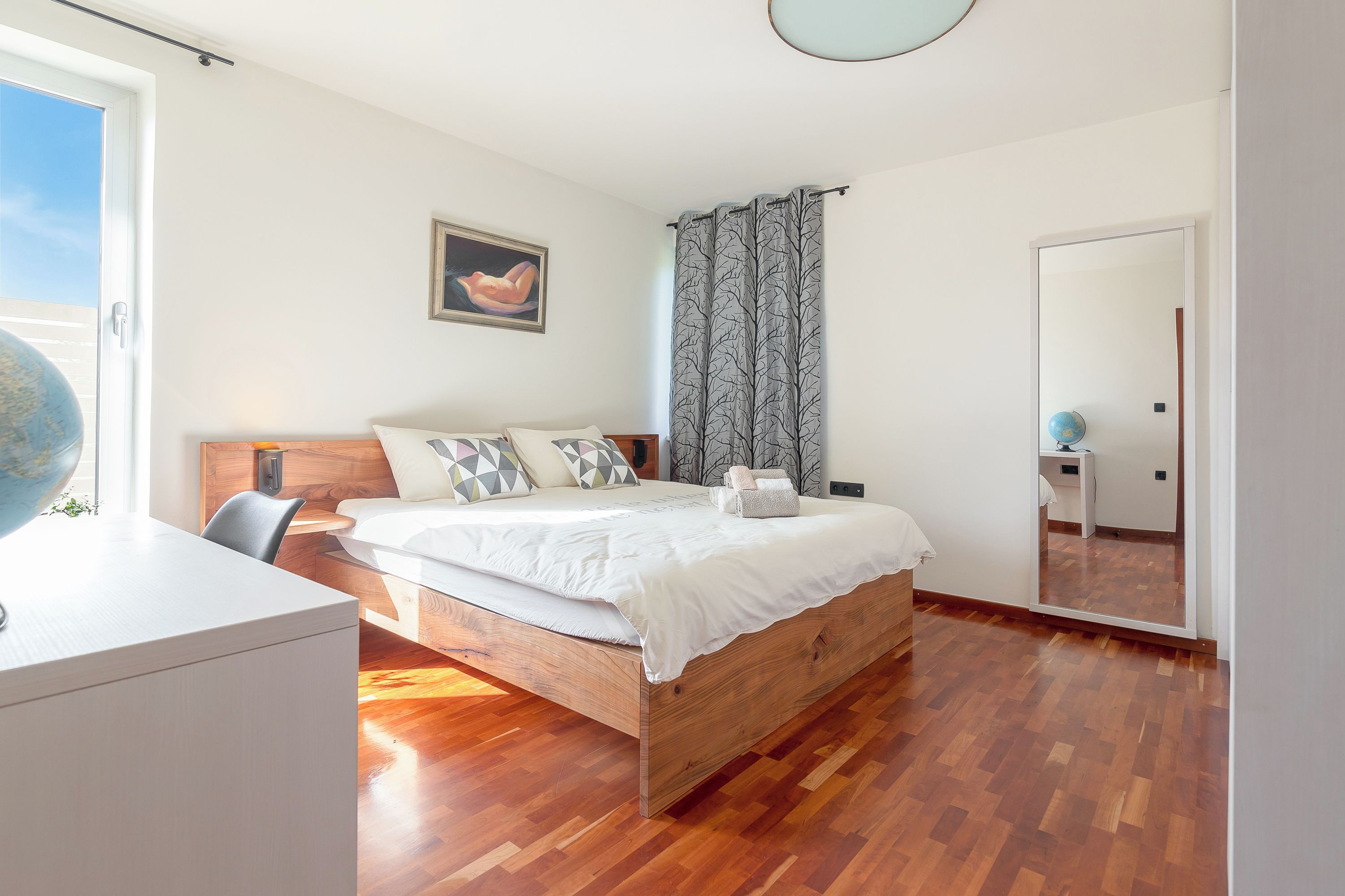 Un dormitorio con una cama de madera, un escritorio, un globo terráqueo y un espejo grande.