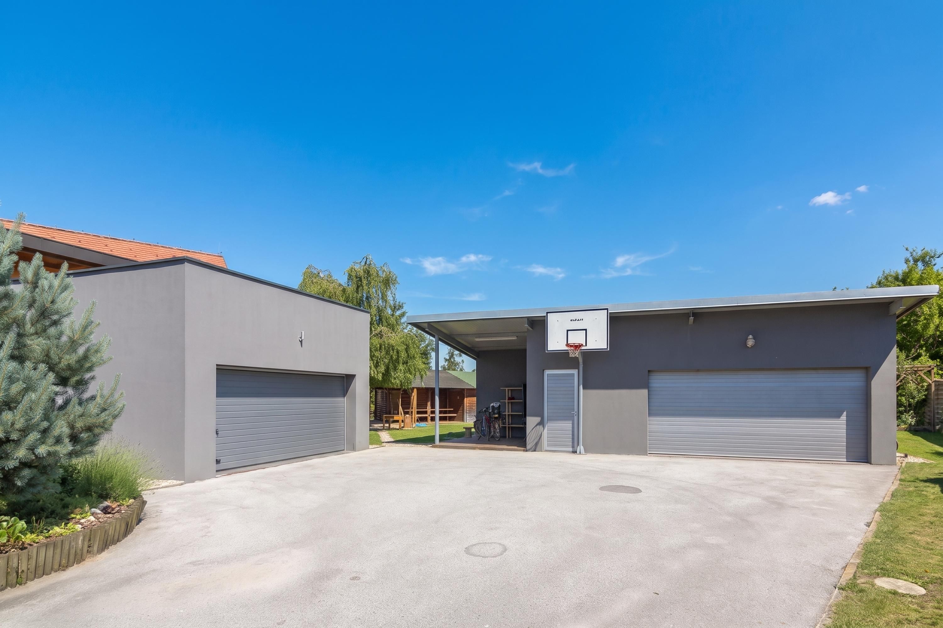 A modern building with two garage doors, a basketball hoop, and a covered driveway.