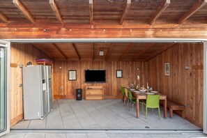 Un garaje con interior de madera, un televisor montado en la pared, un refrigerador, un altavoz y una mesa de comedor con sillas.