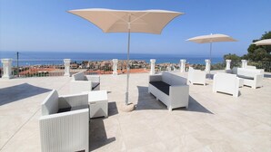A rooftop terrace with white wicker furniture, beige umbrellas, and a view of the sea and cityscape. - Appartamenti Borgo Panoramico N.8 (Tropea)