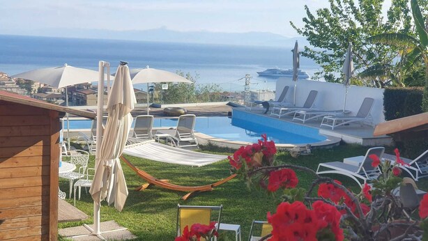 A pool area with lounge chairs and umbrellas, a hammock, and a view of the sea. - Appartamenti Borgo Panoramico N.8 (Tropea)