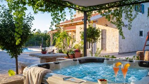 A hot tub with two drinks and a bowl of fruit, surrounded by potted plants and a stone building in the background. - Cozy home in Drnis with sauna (Drnis)