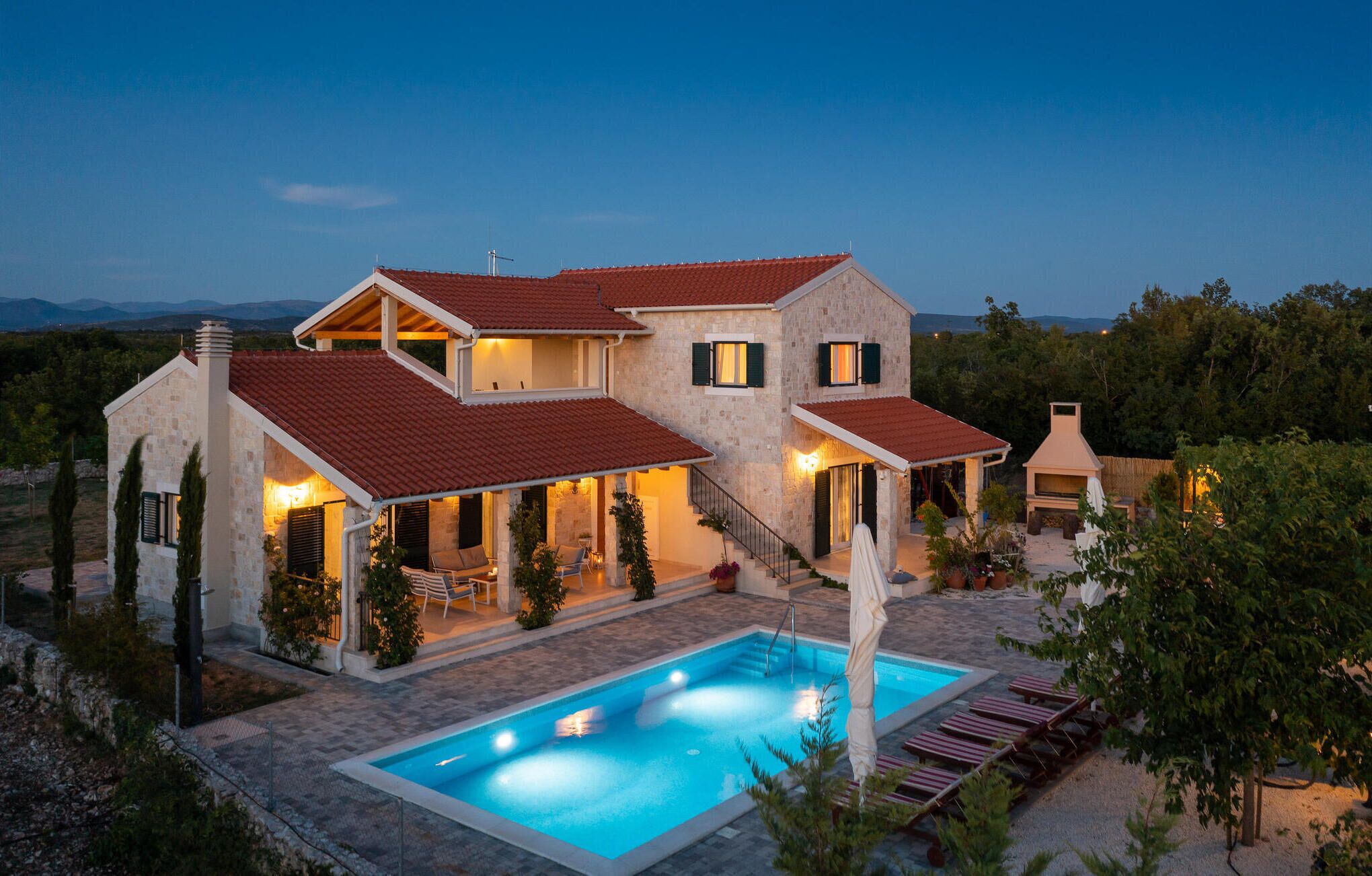 A two-story house with a swimming pool, stone exterior, and red-tiled roof.