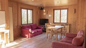 A wooden cabin interior with a red sofa, a dining table with chairs, and a television. - A large chalet for getting together with family, friends or colleagues!  (Cerniat)