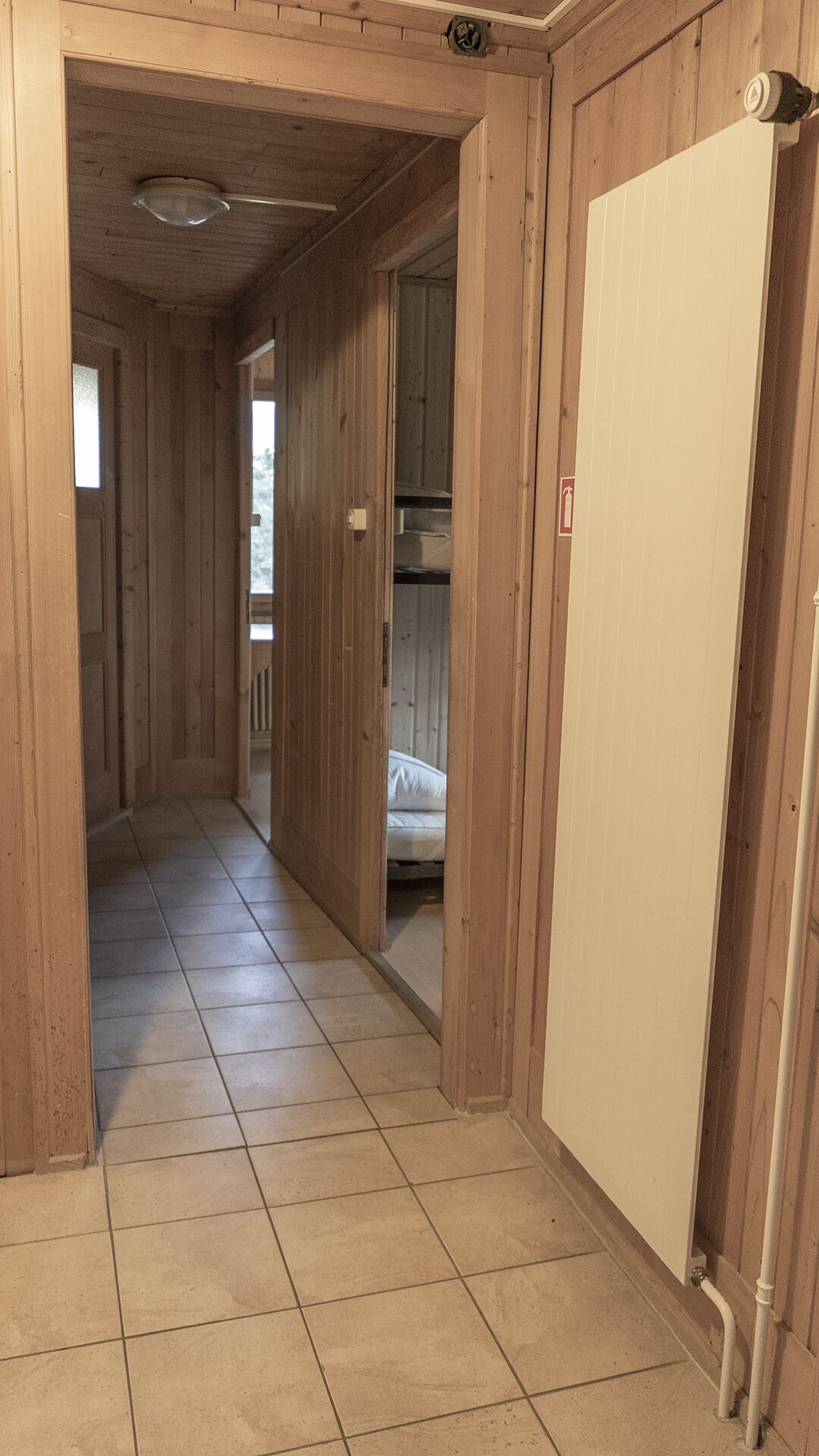 En hall med träpanel och ett klinkergolv som leder till ett rum med en säng.