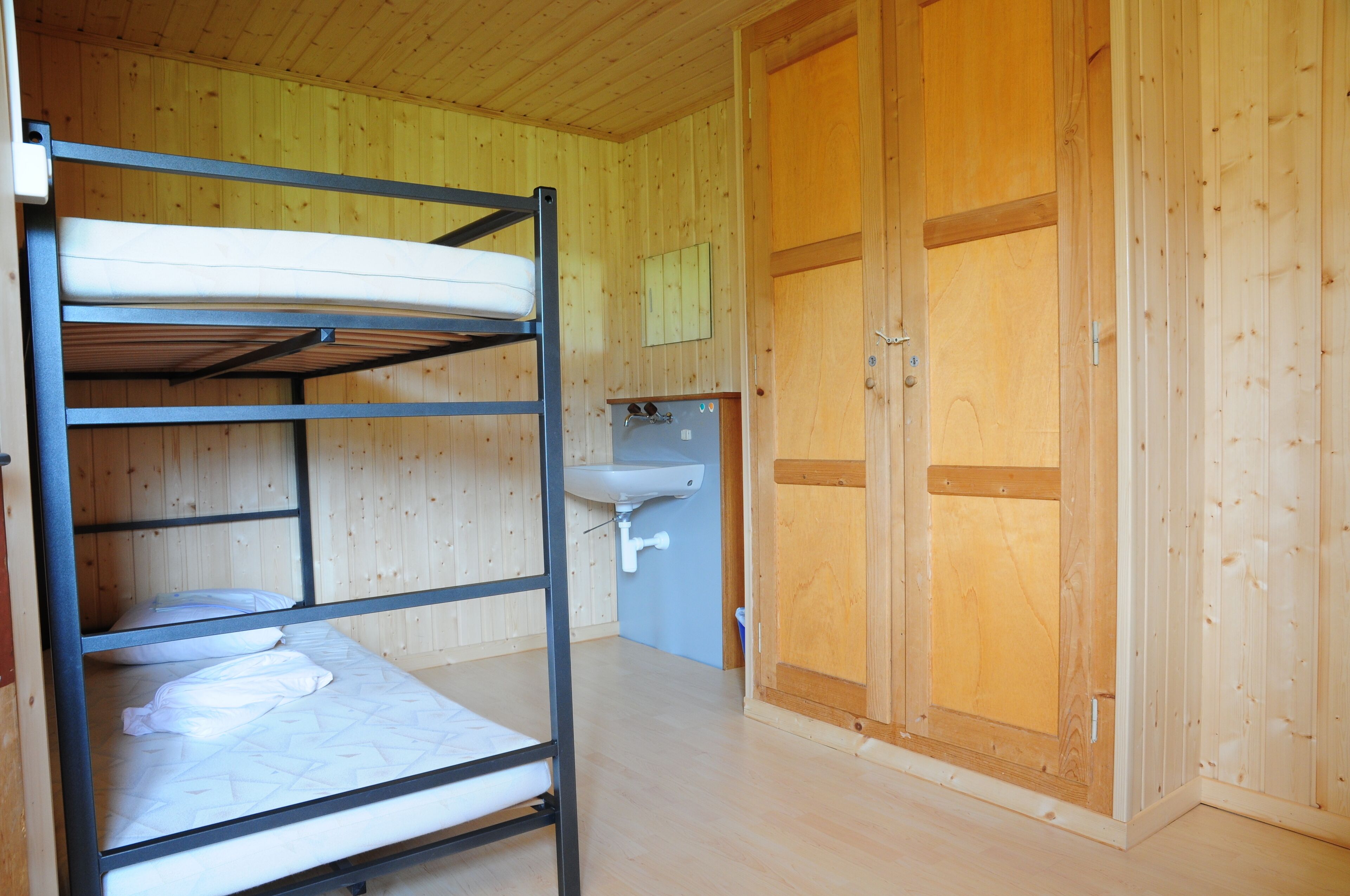 Ein Stockbett mit Waschbecken und einem Holzschrank in einem Zimmer mit Holzwänden.