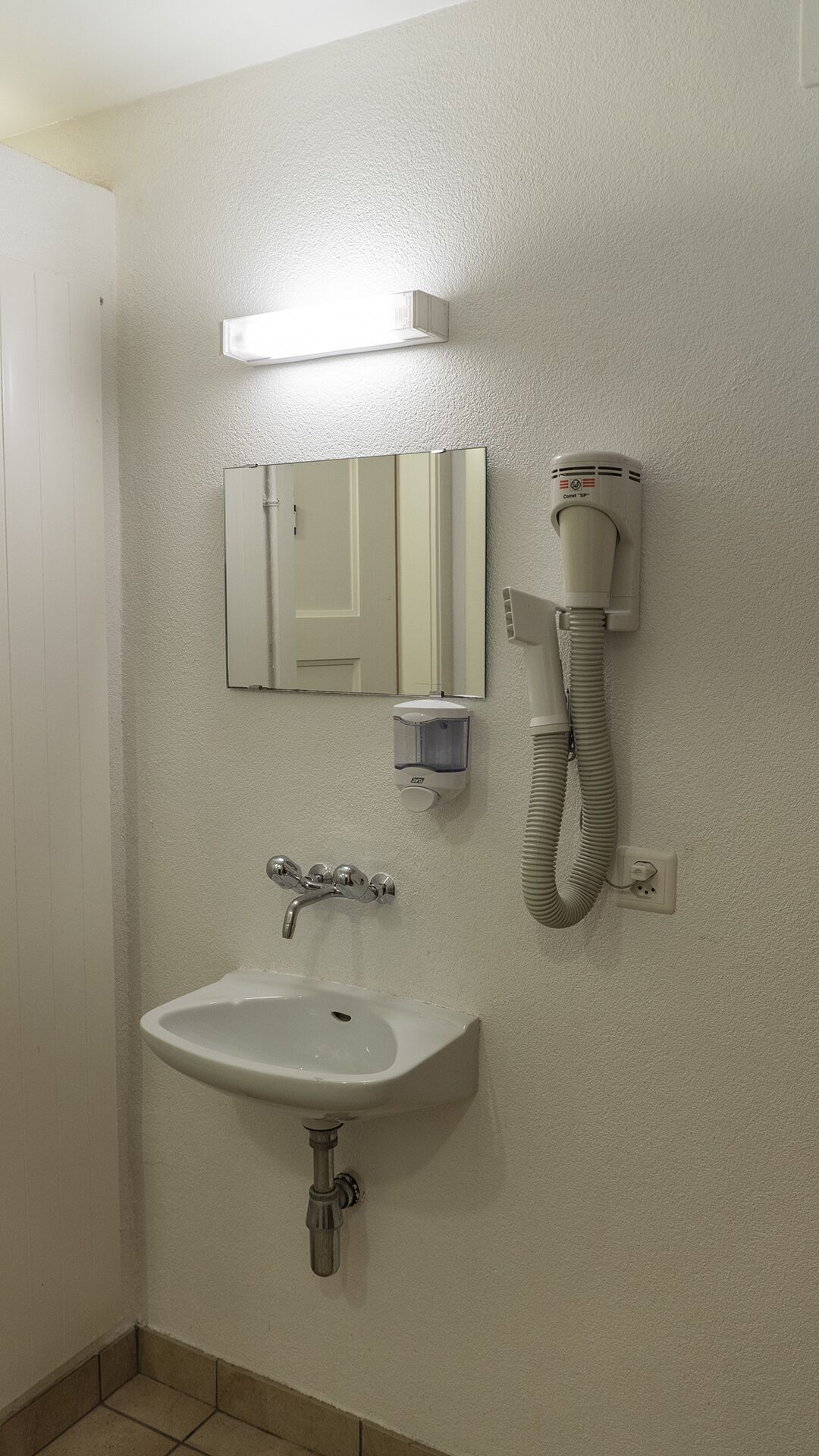 Ein Badezimmer mit einem weißen Waschbecken, einem Spiegel, einem Handtrockner und einem an der Wand montierten Telefon.