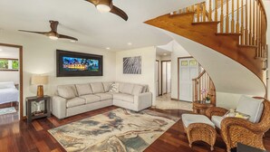 A spacious living area with a wooden staircase, a sectional sofa, a large rug, and wicker furniture. - Oceanfront Hanalei Bay home - Hanalei Surf (Hanalei)