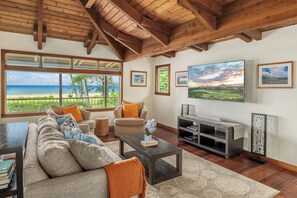 A spacious living room with a large window overlooking a beach, a fireplace, and a flat-screen TV.