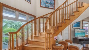 A wooden staircase with a chandelier, framed artwork, and a view of greenery outside. - Oceanfront Hanalei Bay home - Hanalei Surf (Hanalei)