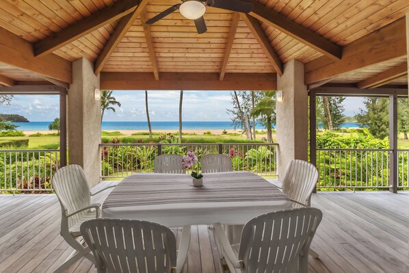 Un espace extérieur abrité, avec une table et des chaises, donnant sur une plage.