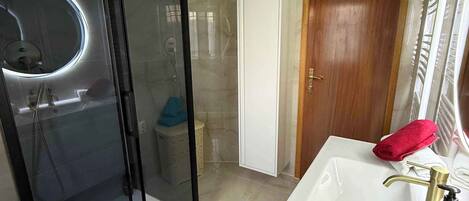 A bathroom with a glass-enclosed shower, a white sink with a gold faucet, and a wooden door.