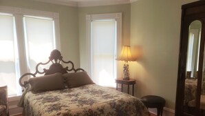 A bedroom with a bed, a nightstand, a lamp, a chair, and a mirror. - NEW VICTORIAN GEM IN GREENPORT (Greenport)