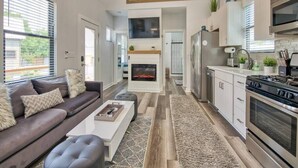 A modern kitchen with a central island, built-in appliances, and a dining area with a sofa and coffee table. - Boutique Tiny Home - River, Fire Pit, Walkable (Waynesville)