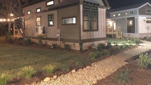 A two-story house with a sloped roof, a front porch, and a small garden area with a gravel path. - Boutique Tiny Home - River, Fire Pit, Walkable (Waynesville)