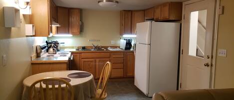 A compact kitchen with wooden cabinets, a refrigerator, a stove, and a dining table with chairs.