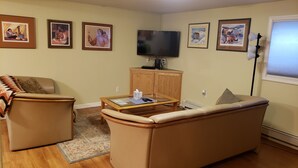 A living room with a beige sofa, a glass coffee table, a television, and framed pictures on the wall. - Property near Pioneer Park, Chena River, and the Carlson Center. Sleeps 4 (Fairbanks)