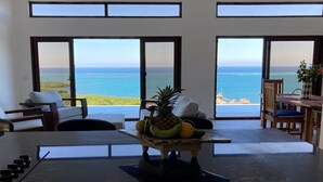 A room with a large table, chairs, and a view of the ocean.