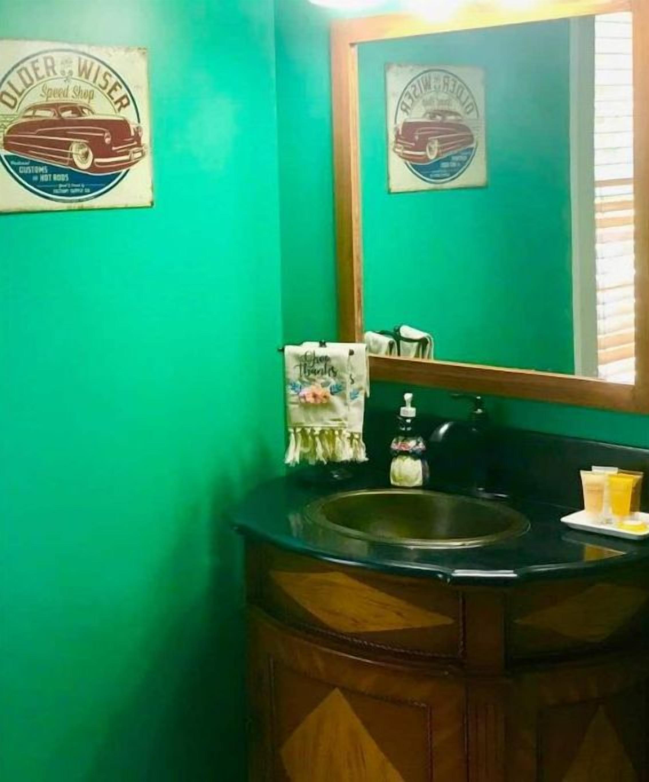 A bathroom with green walls, a wooden vanity, a mirror, and a framed poster on the wall.