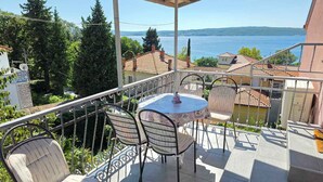 Ein Balkon mit Tisch und Stühlen mit Blick auf einen See, umgeben von Grünflächen und Gebäuden.